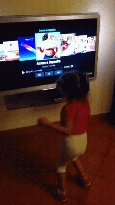 A Little Girl Is Dancing In Front Of A Tv Screen That Says Amore Capoeira GIF
