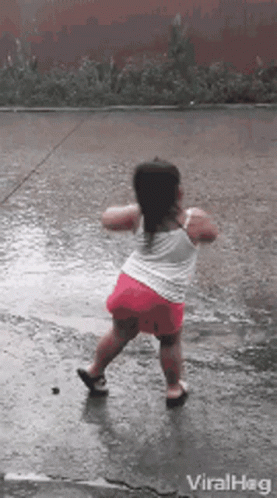 A Little Girl Is Dancing In The Rain On A Wet Sidewalk . GIF