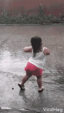 A Little Girl Is Dancing In The Rain On A Wet Sidewalk . GIF