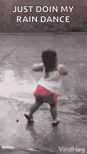 A Little Girl Is Dancing In The Rain On The Sidewalk . GIF