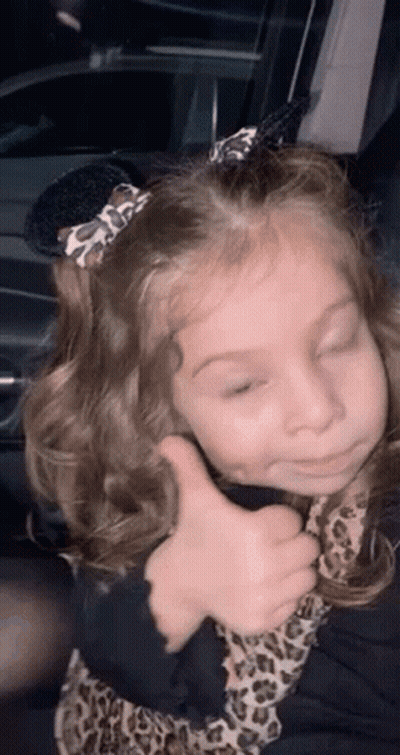 A Little Girl Is Giving A Thumbs Up While Sitting In A Car . GIF