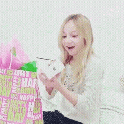 A Little Girl Is Holding A Box In Front Of A Birthday Bag That Says Happy Birthday GIF