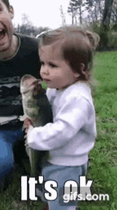 A Little Girl Is Holding A Large Fish In Her Arms . GIF