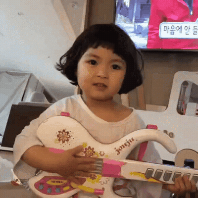 A Little Girl Is Holding A Toy Guitar In Her Hands . GIF
