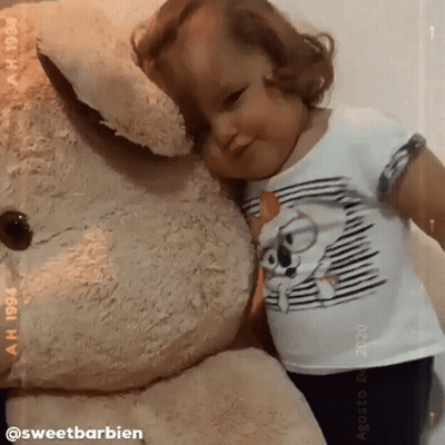 A Little Girl Is Hugging A Giant Teddy Bear GIF