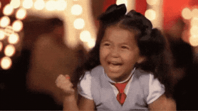 A Little Girl Is Laughing With Her Fist In The Air While Wearing A Vest And Tie . GIF