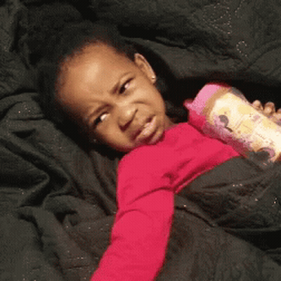 A Little Girl Is Laying On A Bed Holding A Pink Bottle . GIF