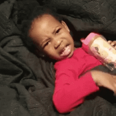 A Little Girl Is Laying On A Bed With A Bottle Of Milk In Her Hand . GIF
