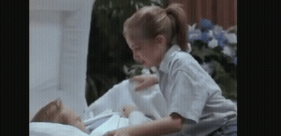 A Little Girl Is Laying On Top Of A Corpse In A Hospital Bed . GIF