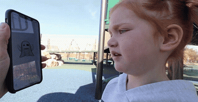 A Little Girl Is Looking At A Phone With A Ghost On The Screen GIF