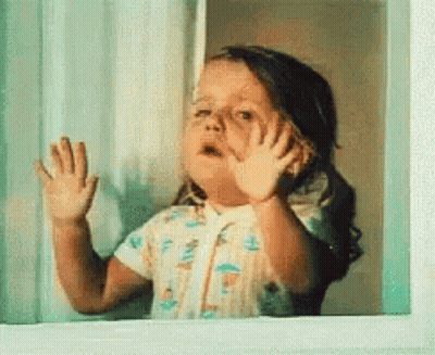 A Little Girl Is Looking Out Of A Window And Waving Her Hands . GIF