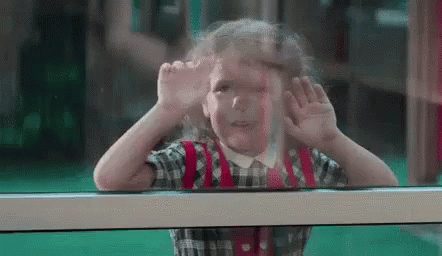 A Little Girl Is Looking Out Of A Window . GIF