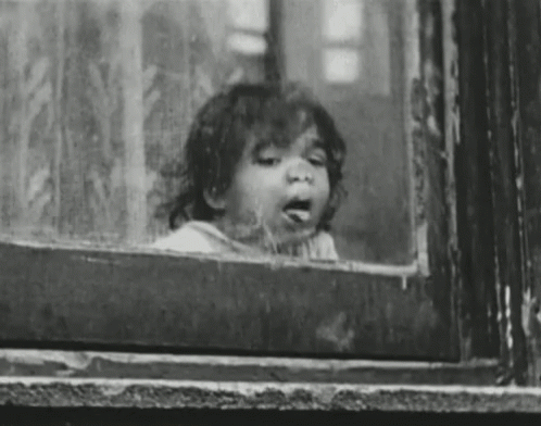 A Little Girl Is Looking Out Of A Window . GIF
