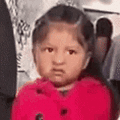 A Little Girl Is Making A Funny Face While Wearing A Red Coat . GIF