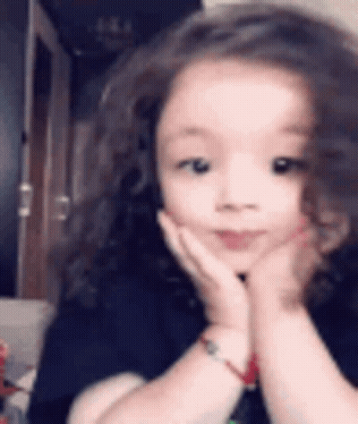 A Little Girl Is Making A Funny Face With Her Hands On Her Face . GIF
