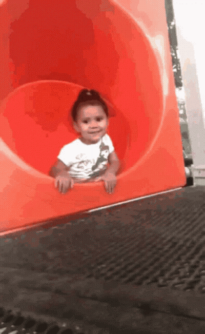 A Little Girl Is Playing On A Red Slide GIF
