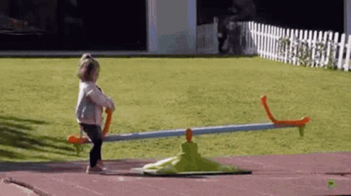 A Little Girl Is Playing With A Seesaw In A Yard . GIF