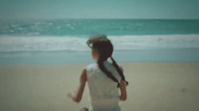 A Little Girl Is Running On A Beach Near The Ocean . GIF
