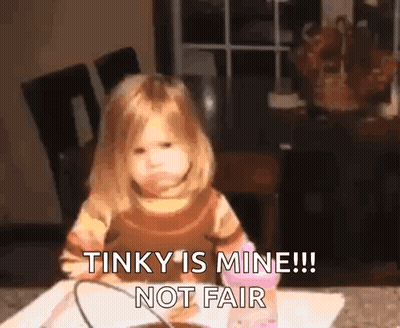 A Little Girl Is Sitting At A Table And Making A Funny Face And Saying That Tinky Is Mine !! Not Fair . GIF