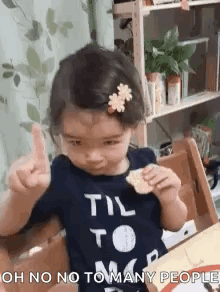A Little Girl Is Sitting At A Table Eating A Cracker And Giving A Thumbs Up . GIF