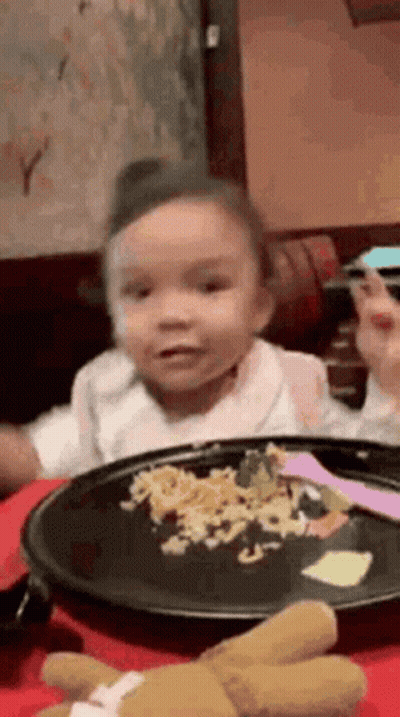 A Little Girl Is Sitting At A Table Eating A Plate Of Food . GIF