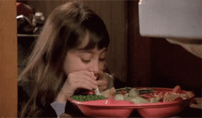 A Little Girl Is Sitting At A Table Eating A Plate Of Food With A Fork . GIF