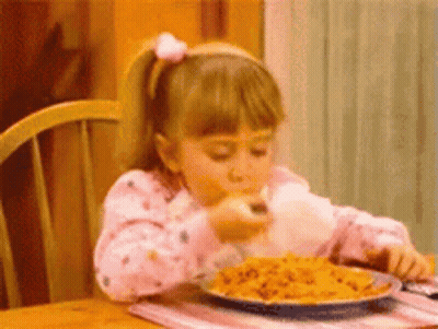 A Little Girl Is Sitting At A Table Eating A Plate Of Pasta . GIF