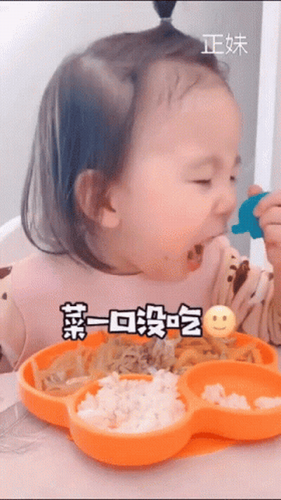 A Little Girl Is Sitting At A Table Eating Food From An Orange Plate With A Smiley Face On It . GIF