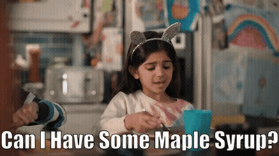 A Little Girl Is Sitting At A Table With A Cup Of Maple Syrup GIF