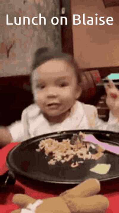 A Little Girl Is Sitting At A Table With A Plate Of Food And A Teddy Bear . GIF