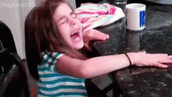 A Little Girl Is Sitting At A Table With Her Arms Outstretched And Screaming . GIF