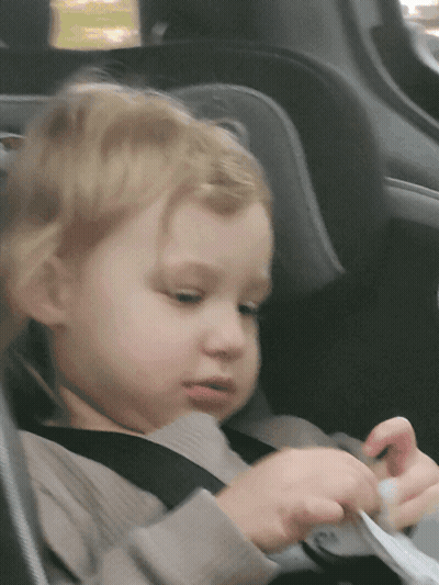 A Little Girl Is Sitting In A Car Seat With A Seat Belt On GIF