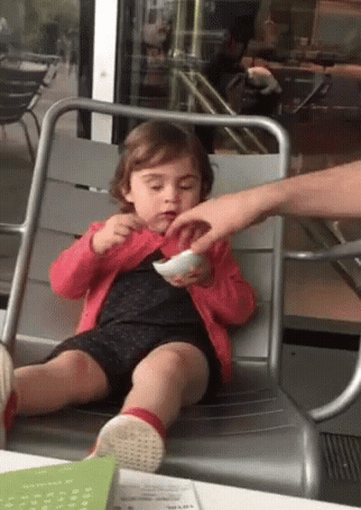 A Little Girl Is Sitting In A Chair Eating A Bowl Of Food GIF