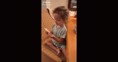 A Little Girl Is Sitting In A Chair Eating A Cookie . GIF
