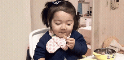 A Little Girl Is Sitting In A High Chair Eating A Piece Of Food . GIF
