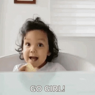 A Little Girl Is Sitting In A High Chair Eating A Piece Of Food And Giving The Middle Finger . GIF