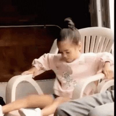 A Little Girl Is Sitting In A White Chair . GIF
