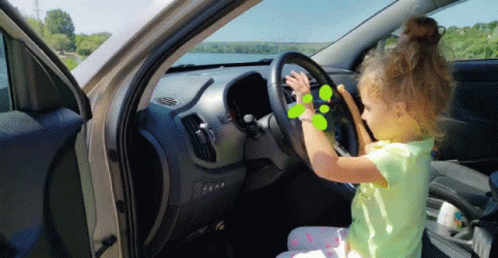 A Little Girl Is Sitting In The Driver 'S Seat Of A Car Playing With The Steering Wheel GIF