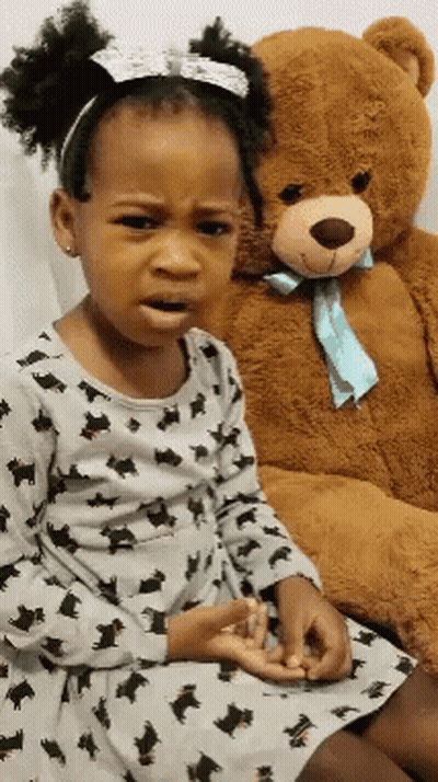 A Little Girl Is Sitting Next To A Teddy Bear And Making A Sad Face GIF