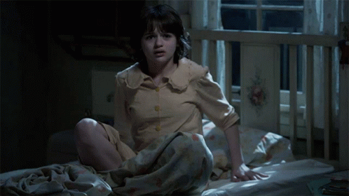 A Little Girl Is Sitting On A Bed With A Blanket Over Her Head GIF