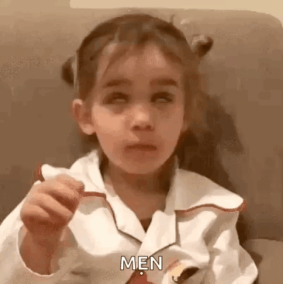 A Little Girl Is Sitting On A Couch Eating A Sandwich And Making A Face . GIF