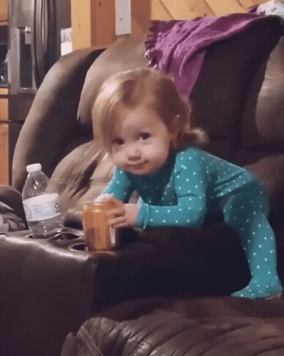 A Little Girl Is Sitting On A Couch Holding A Bottle Of Water GIF