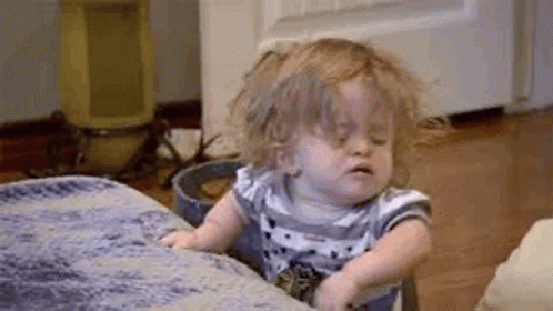 A Little Girl Is Sitting On A Couch With Her Eyes Closed And Making A Funny Face . GIF