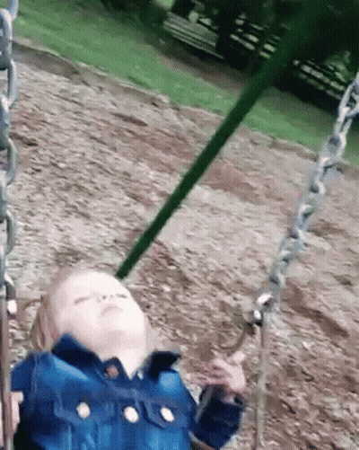 A Little Girl Is Sitting On A Swing In A Park With Her Eyes Closed . GIF