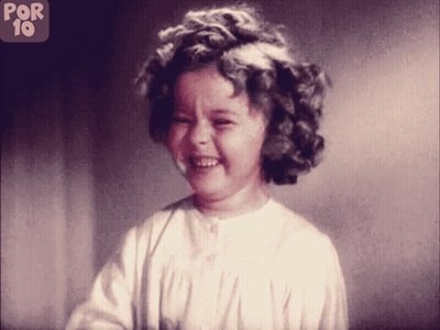 A Little Girl Is Smiling In Front Of A Sign That Says Por 10 On It GIF