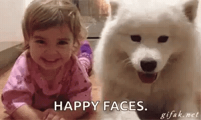 A Little Girl Is Smiling While Laying Next To A White Dog . GIF