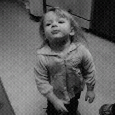 A Little Girl Is Standing In A Kitchen And Making A Funny Face In A Black And White Photo . GIF