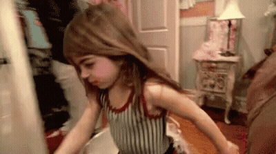 A Little Girl Is Standing In A Room With Her Hair In The Air . GIF