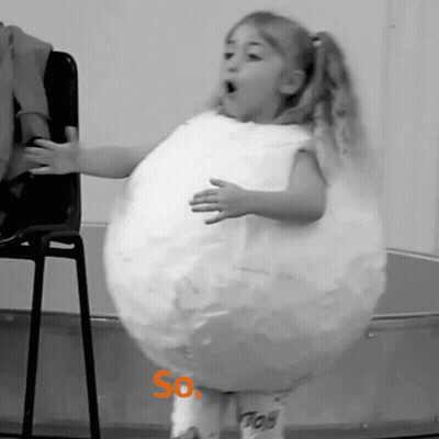 A Little Girl Is Standing In Front Of A Chair Wearing A Costume That Looks Like A Balloon With The Word So On It GIF