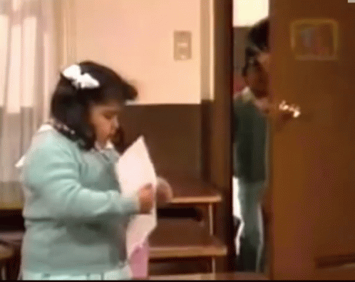 A Little Girl Is Standing In Front Of A Door Holding A Piece Of Paper .. GIF